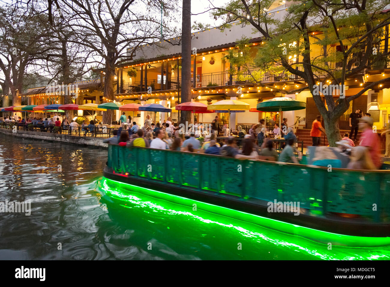 San Antonio River Walk - - Un barco turístico sobre el río San Antonio pasando restaurantes al anochecer; San Antonio Riverwalk de San Antonio, Texas, EE.UU. Foto de stock