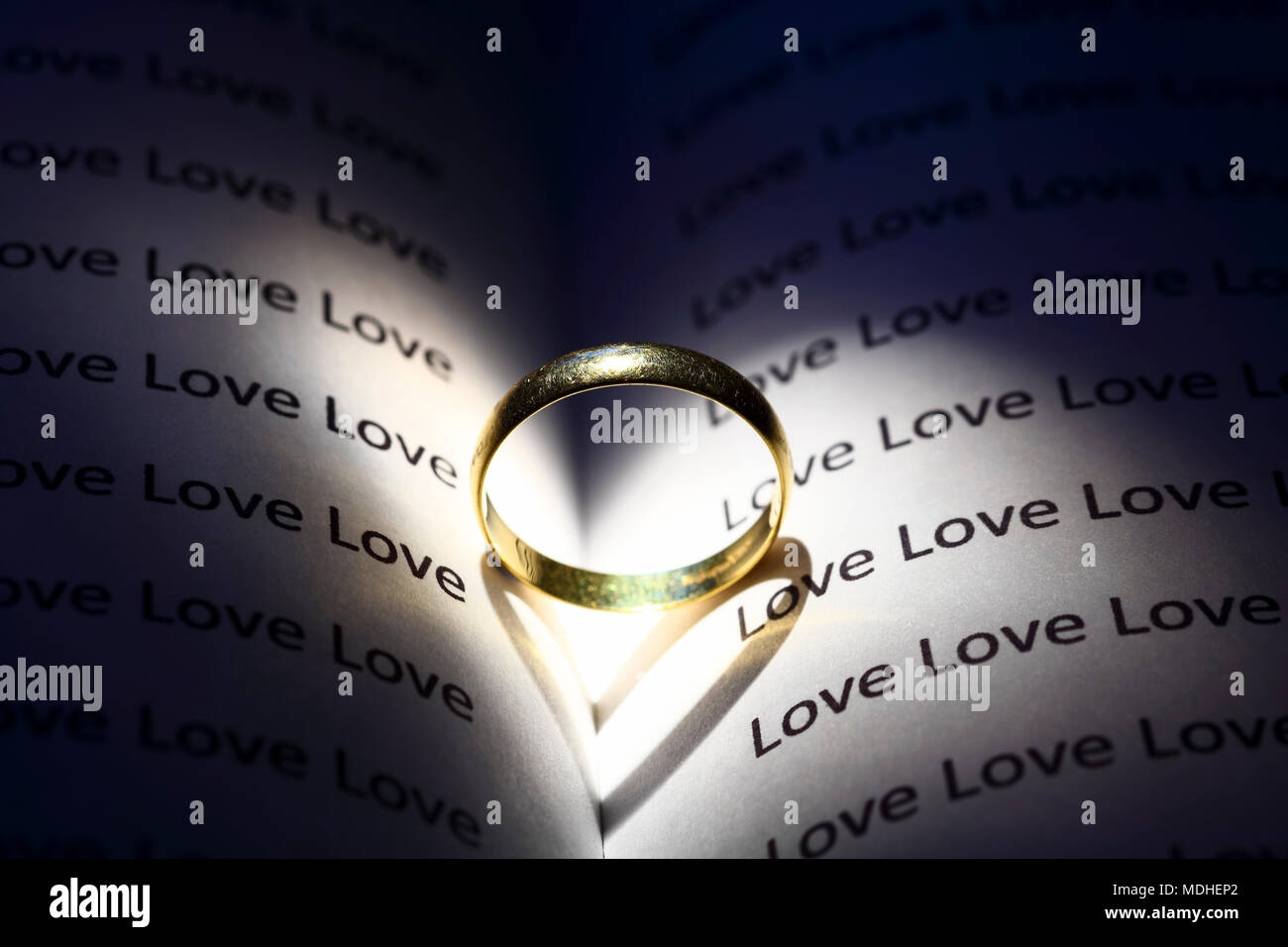 Único anillo de bodas de oro sobre un libro abierto con la palabra amor  repetidas y la silueta de una forma corazón en las páginas Fotografía de  stock - Alamy