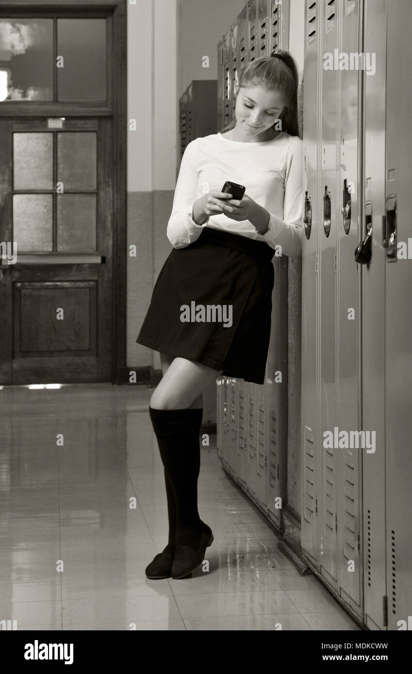 Colegiala con su teléfono celular en el pasillo de la escuela secundaria Foto de stock
