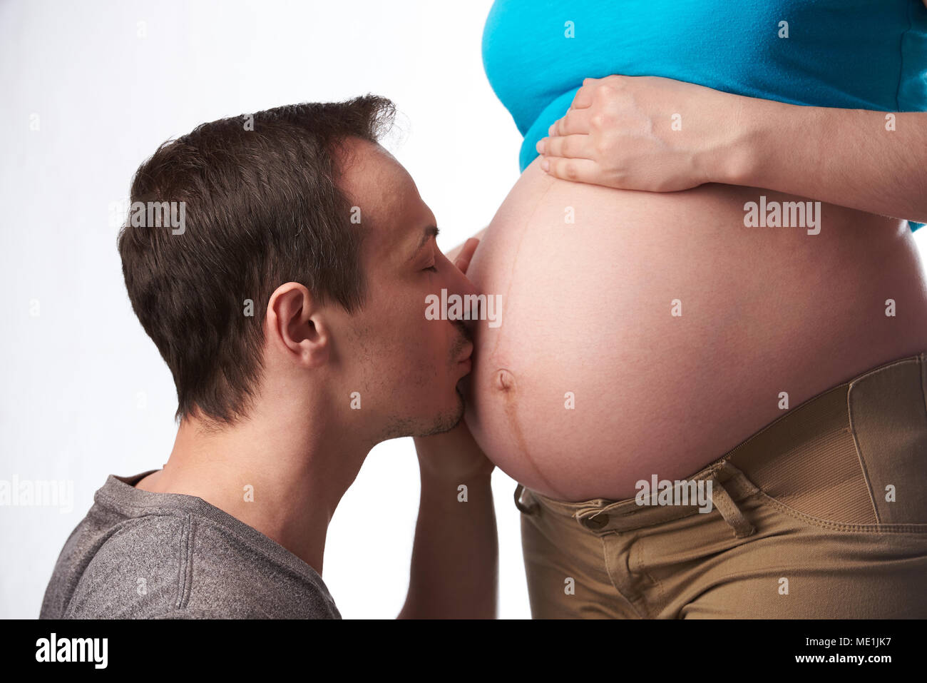 Joven besar el vientre de la mujer embarazada aislado sobre fondo blanco. Foto de stock