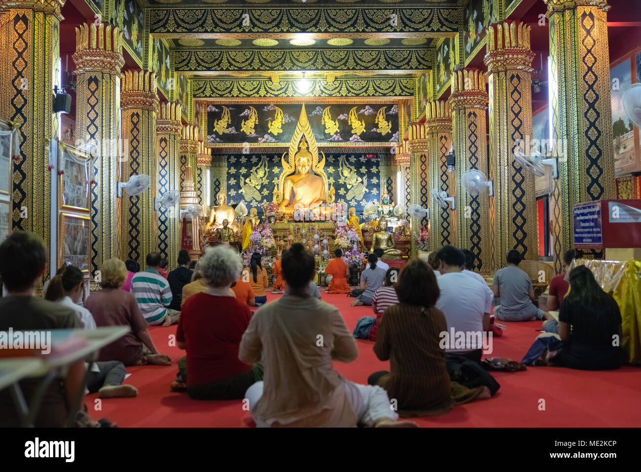 CHIANG MAI, Tailandia - El 29 de enero de 2018; los devotos y monjes dentro de un templo budista sentada en el piso cantando y orando delante grandes Buddh dorado Foto de stock