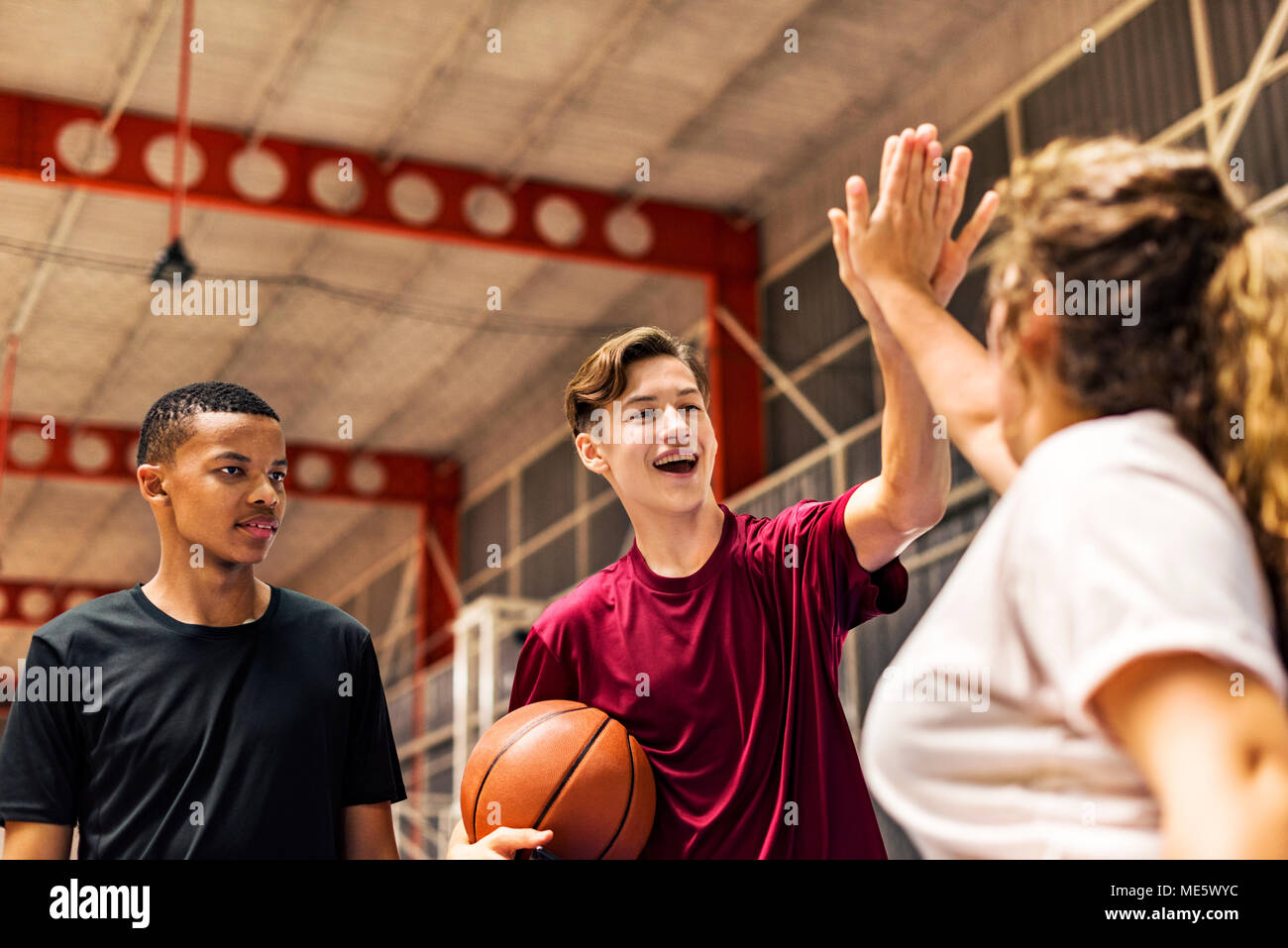 Grupo de Amigos adolescente en una cancha de baloncesto dándose mutuamente una alta cinco Foto de stock