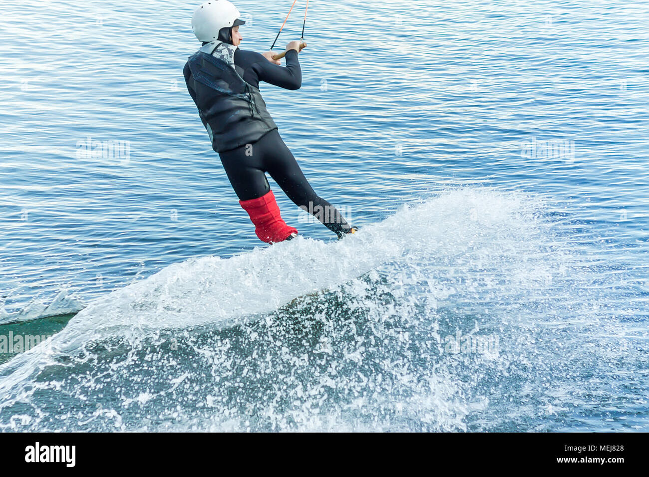 Wakeboarder salta desde un trampolín detrás de una cuerda y hace una ola en el agua. Foto de stock