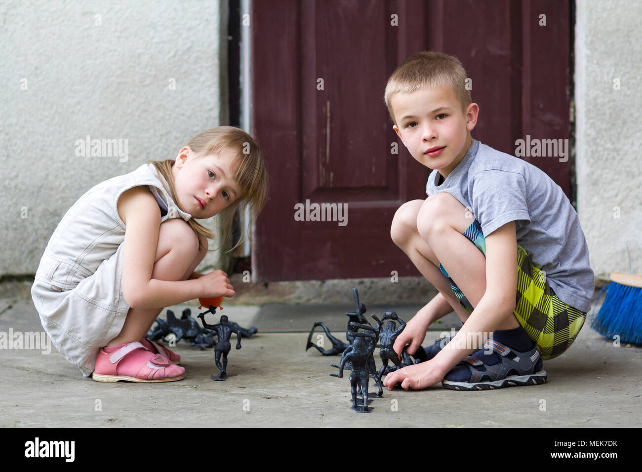 Dos niños lindo rubia bonita niña preescolar y guapo muchacho jugar afuera  con juguetes de plástico en un cálido día de verano sobre fondo de casa  antigua. Carel Fotografía de stock -