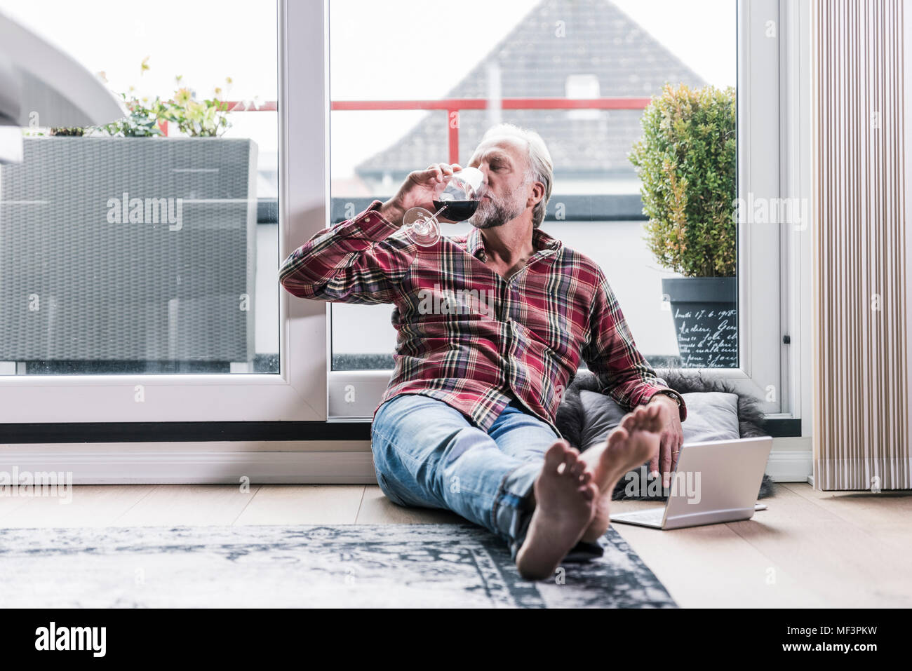 Relajante del Hombre Descalzo en el piso en casa bebiendo una copa de vino tinto Foto de stock