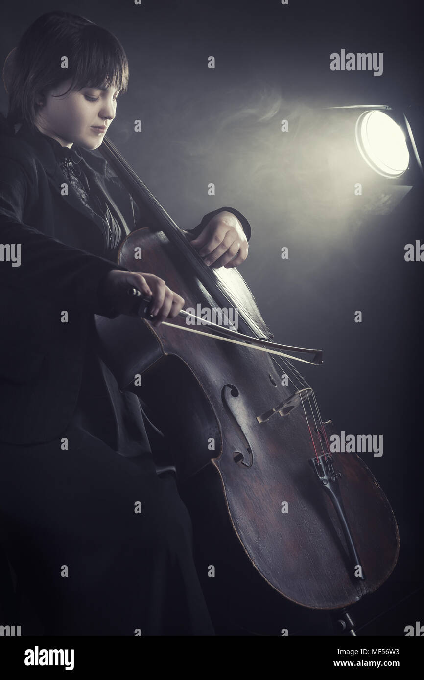 La violonchelista tocando música clásica en el cello contra un fondo negro Foto de stock