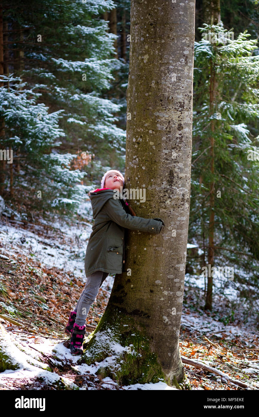 Chica abrazando el árbol en el bosque en invierno Foto de stock