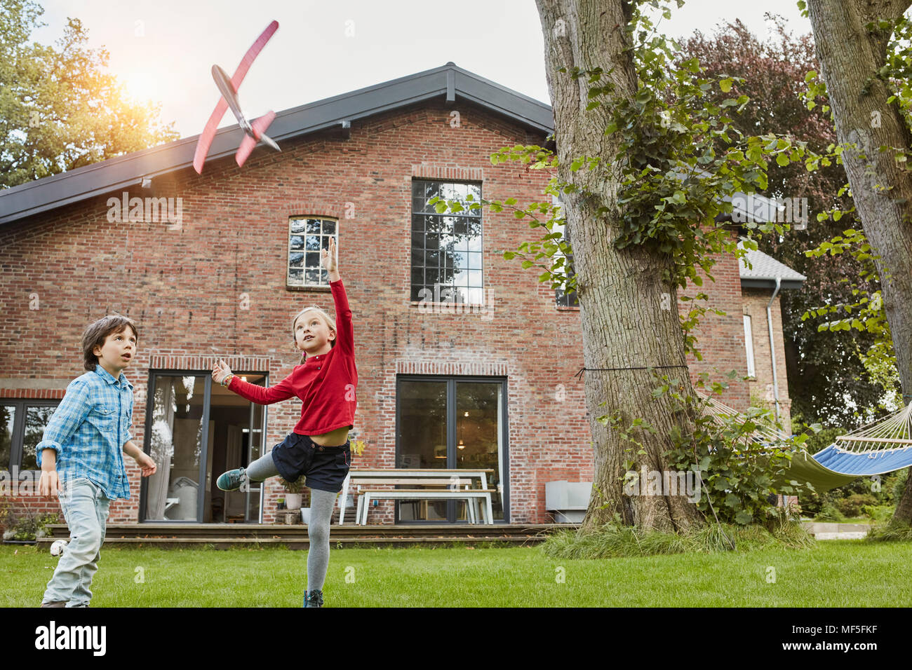 Dos niños jugando con el avión de juguete en el jardín de su casa Foto de stock