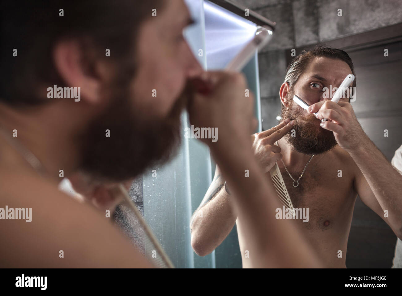 Retrato del hombre barbado mirando su imagen reflejada durante el afeitado Foto de stock