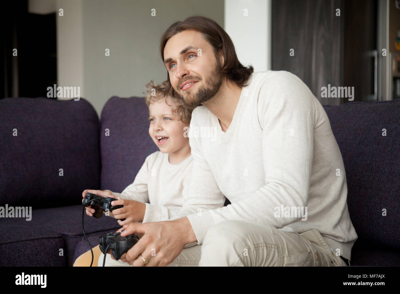 Padre e hijo celebración joysticks disfrutando jugar video juego togeth Foto de stock