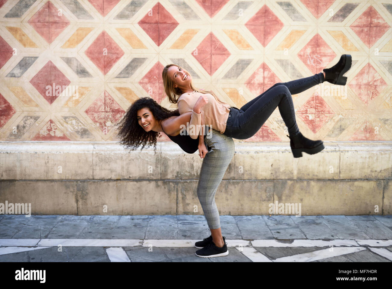 Laughing mujer que llevaba a su mejor amiga piggyback Foto de stock