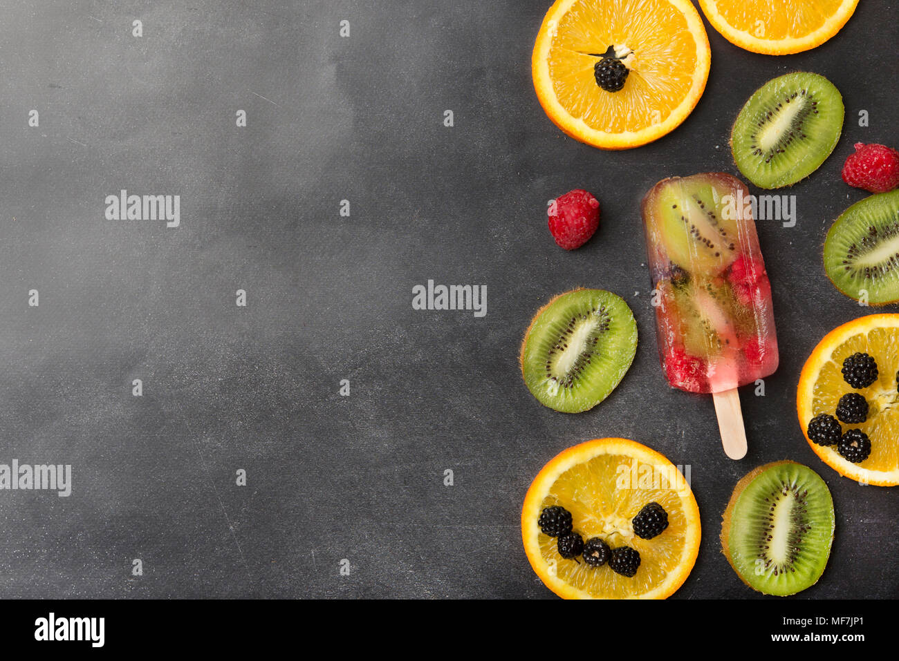 Bayas, frutas en rebanadas y kiwi berry popsicle sobre fondo gris Foto de stock