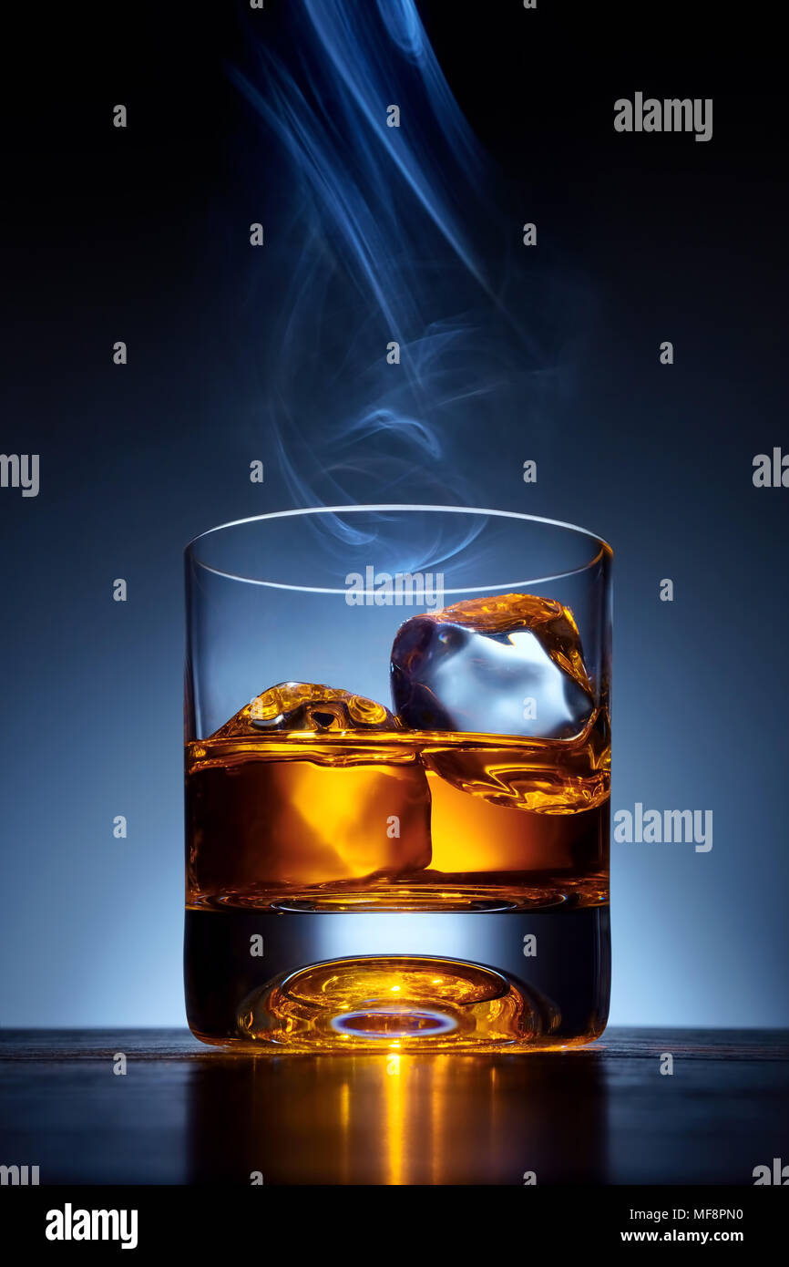 Single Malt Whiskey en un vaso con hielo en una mesa de bar de madera con el humo del cigarrillo en la parte superior del cristal Foto de stock