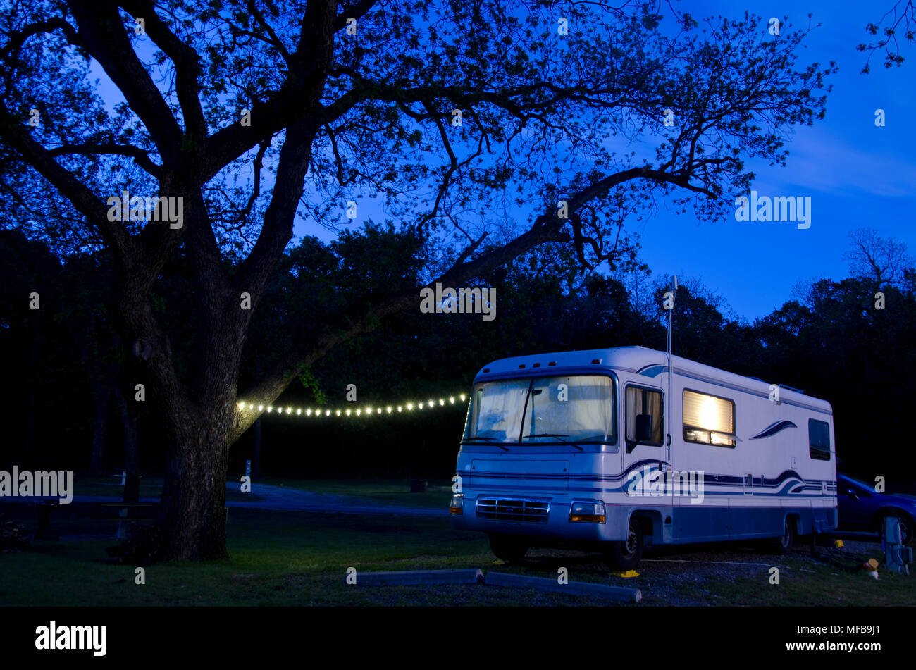 Una gran autocaravana situada bajo un enorme árbol de pacana, iluminó como cae la noche en el camping. Foto de stock