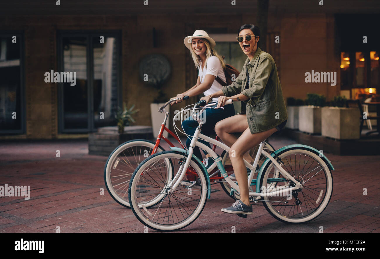 Amigas montando sus bicicletas en las calles de la ciudad. Dos mujeres disfrutando de su paseo en bicicleta. Foto de stock