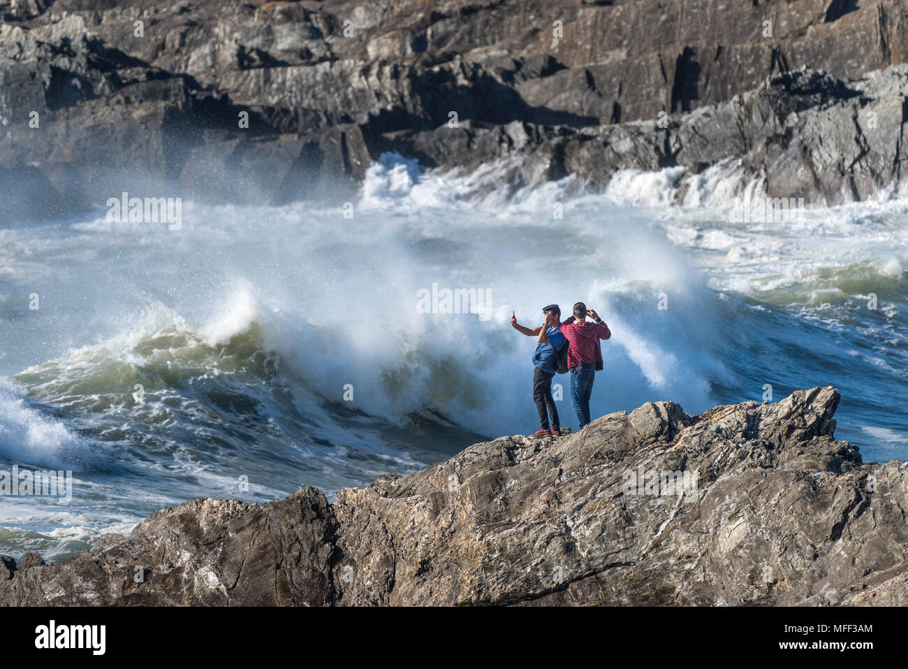 Los turistas de pie sobre las rocas tomando fotografías como grandes olas que rompen en la orilla en poco Fistral en Newquay, Cornwall. Foto de stock