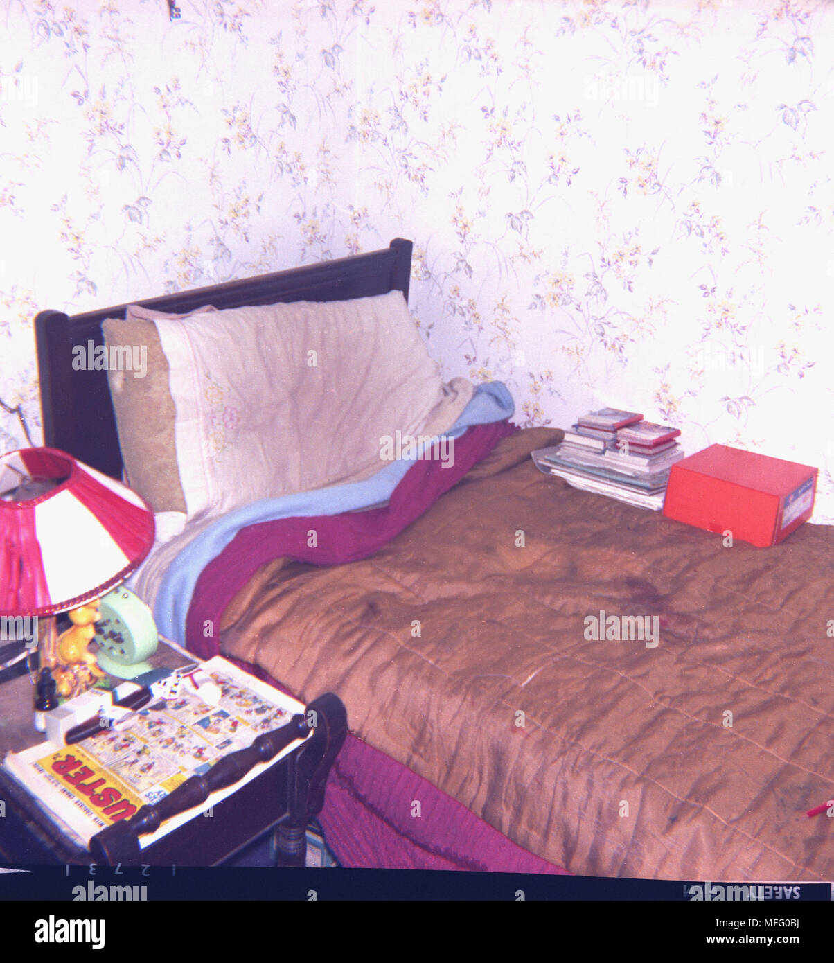 1970 La imagen muestra un desaliñado, desordenado y cama individual en una esquina de la habitación, con una manta marrón brillante sobre ella, y póngalo con una Buster comic sobre la mesita de noche, Inglaterra, Reino Unido. Foto de stock