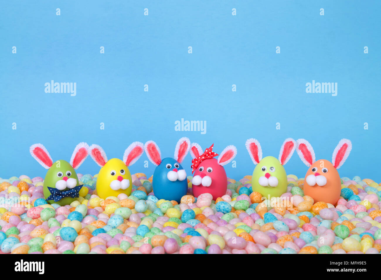 Conejitos de Pascua artesanales hechos de huevos de plástico de color pastel permanente Jelly Beans con un fondo de color azul claro. Pascua de diversión en línea con espacio de copia Foto de stock