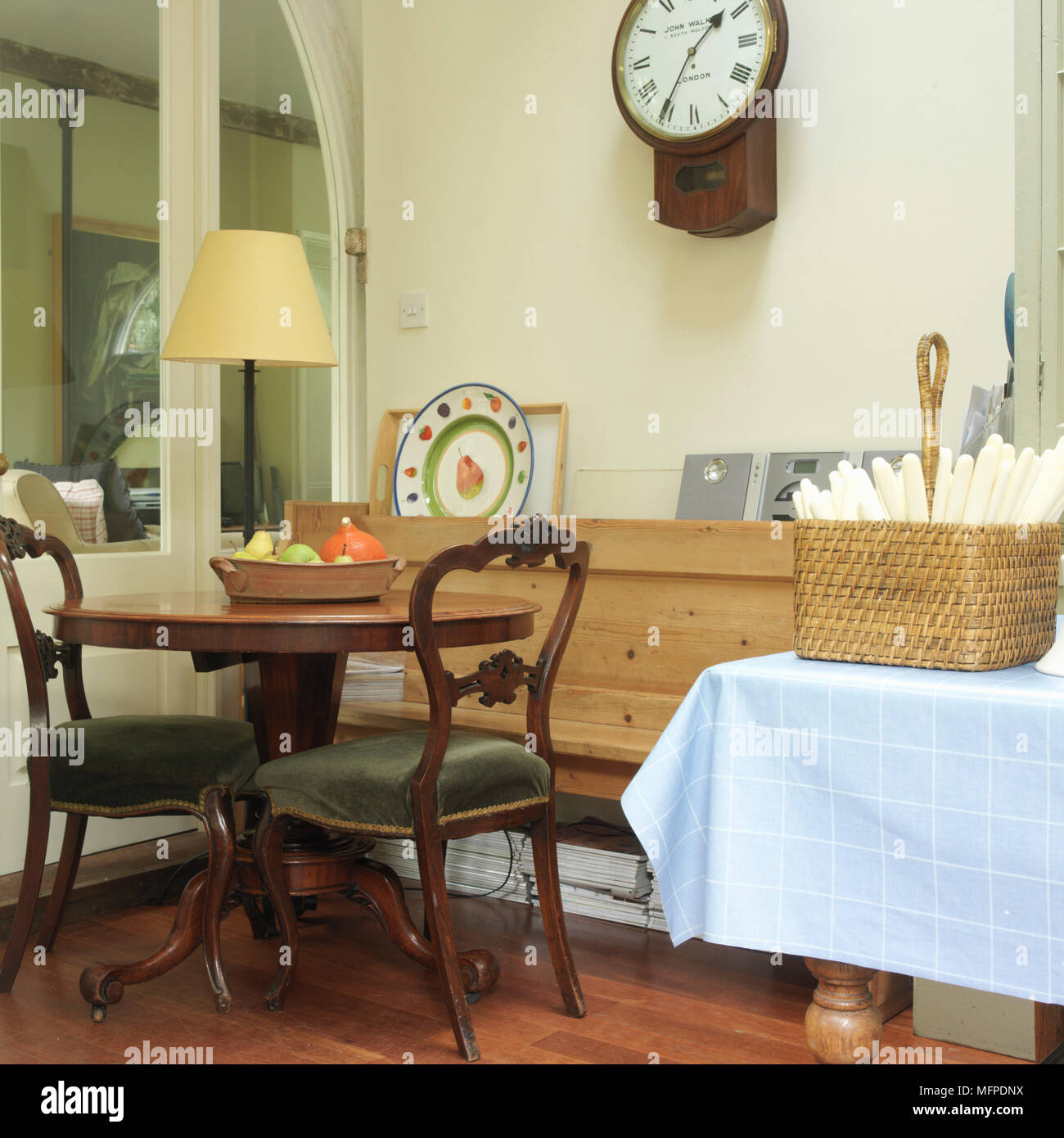 Un comedor de tradicional con una pequeña mesa de comedor redonda de madera y sillas con tapicería verde, un reloj de pared y una mesa de con w Fotografía