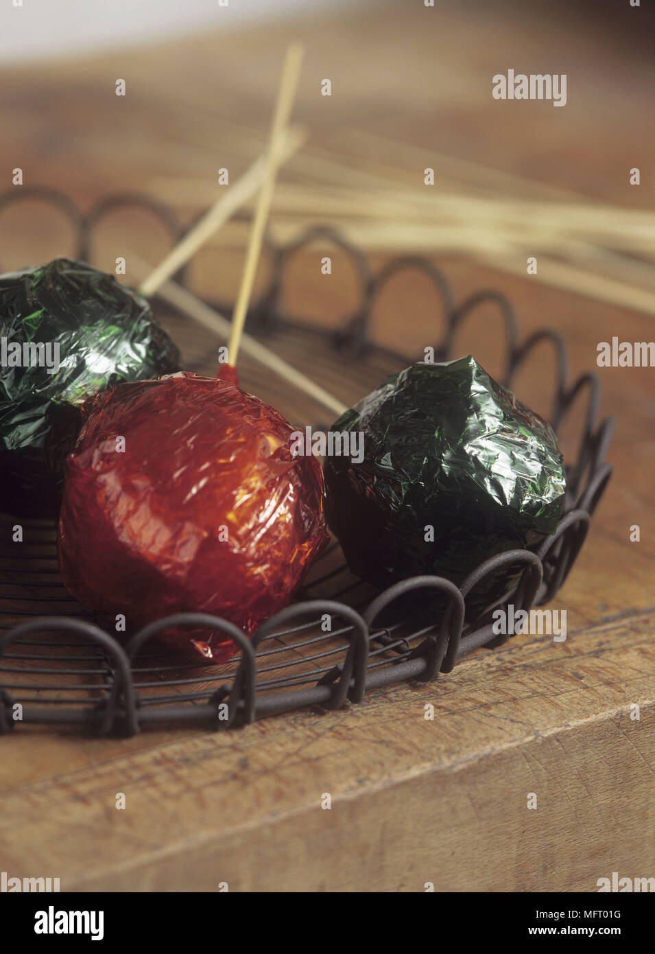 Tres manzanas de caramelo envuelto en celofán rojo y verde en una bandeja en el viejo banco de madera arriba Foto de stock