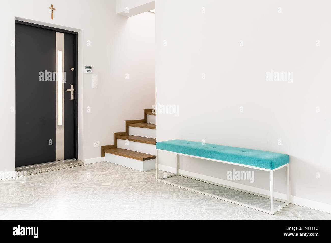 Puerta frontal negro, escaleras y una banqueta tapizados de color turquesa en un hall de entrada interior blanco Foto de stock