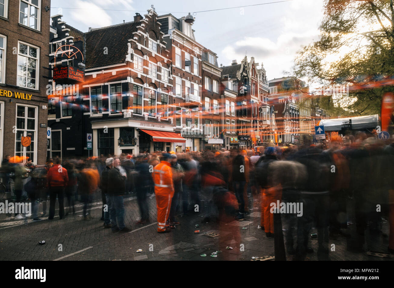 Amsterdam, Holanda - 27 de abril, 2017: calles de Amsterdam, lleno de gente en naranja durante la celebración del Día de Reyes. La gente borrosa al atardecer w Foto de stock
