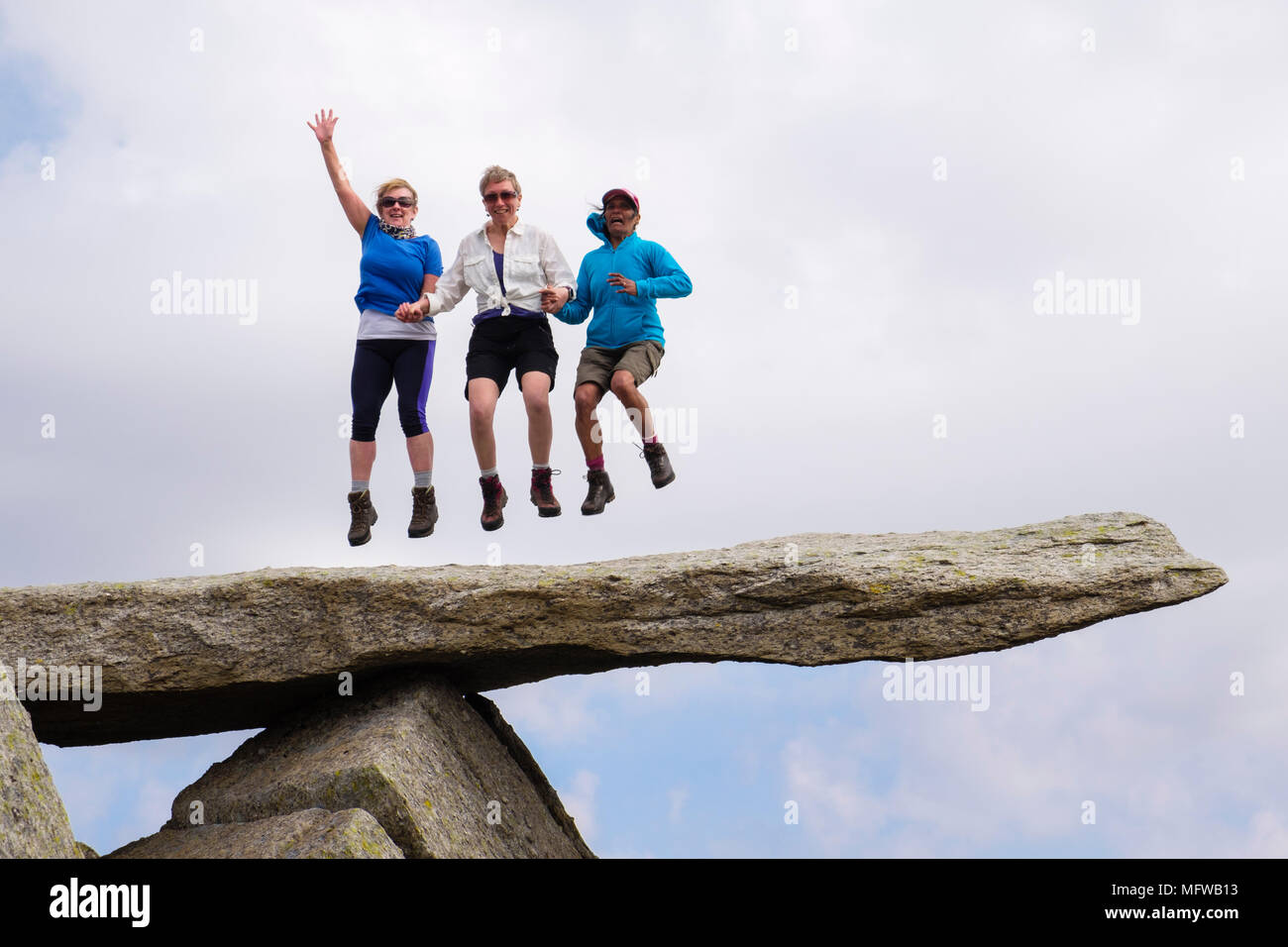 Tres excursionistas felices frente a saltar para la alegría en la losa de roca voladiza en la montaña Glyder Fach en el Parque Nacional de Snowdonia. Gales Reino Unido Foto de stock