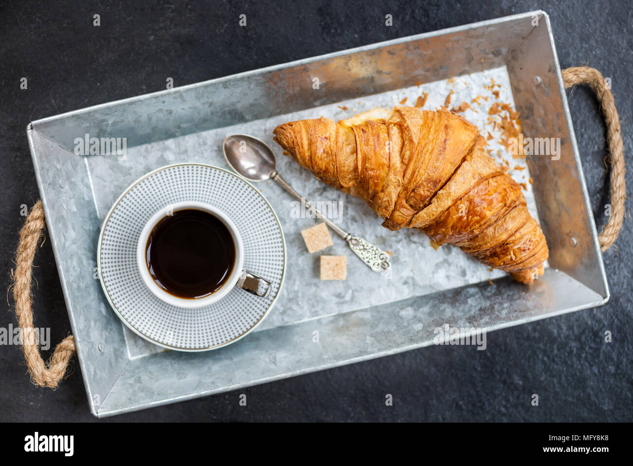 Desayuno ligero desde croissants frescos y una taza de café en la bandeja gris Foto de stock