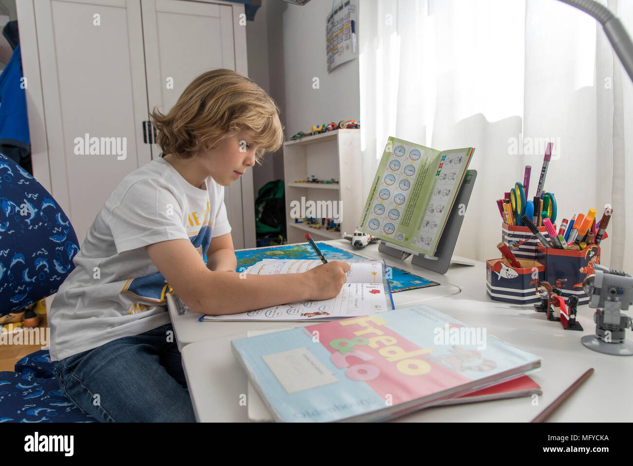 El muchacho, estudiante de primaria, de 8 años, aprende para la escuela, en casa, hace los deberes, Foto de stock