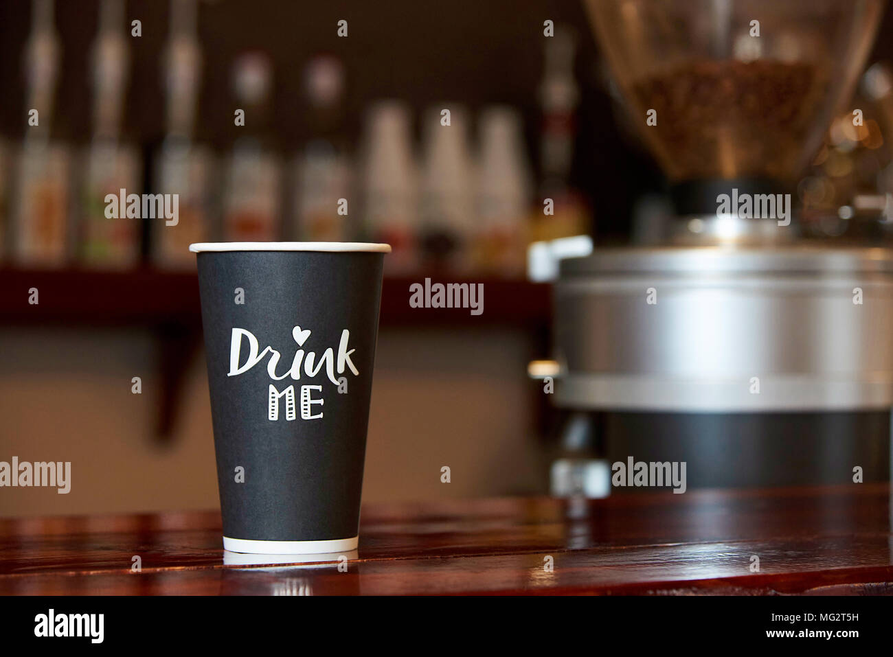 Un vaso de papel de café sobre un contador de madera contra el telón de fondo de un bar borrosa. Foto de stock