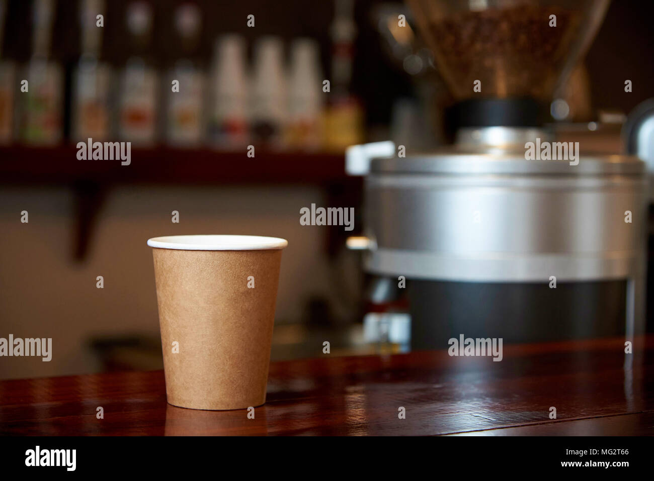 Un vaso de papel de café sobre un contador de madera contra el telón de fondo de un bar borrosa. Foto de stock