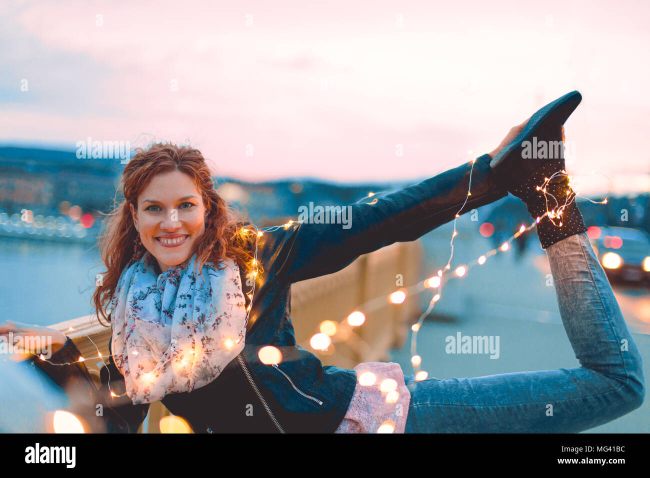Joven pelirroja mujer posando con las luces de hadas afuera y sonrisa, teal y estilo naranja Foto de stock