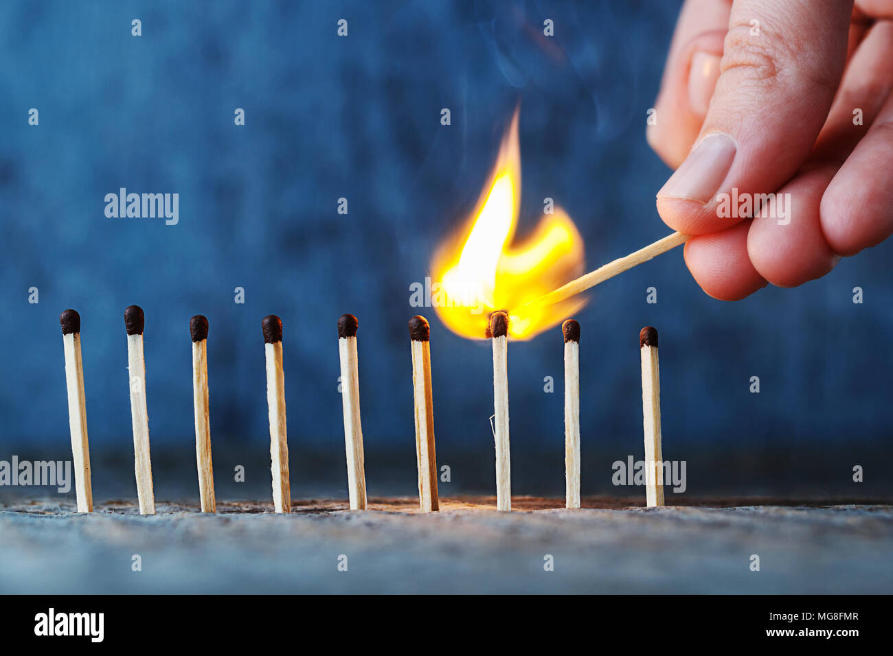 Coincidencias en una fila sobre un fondo de madera, una mano con una  cerilla ardiendo prende fuego a otro partido Fotografía de stock - Alamy
