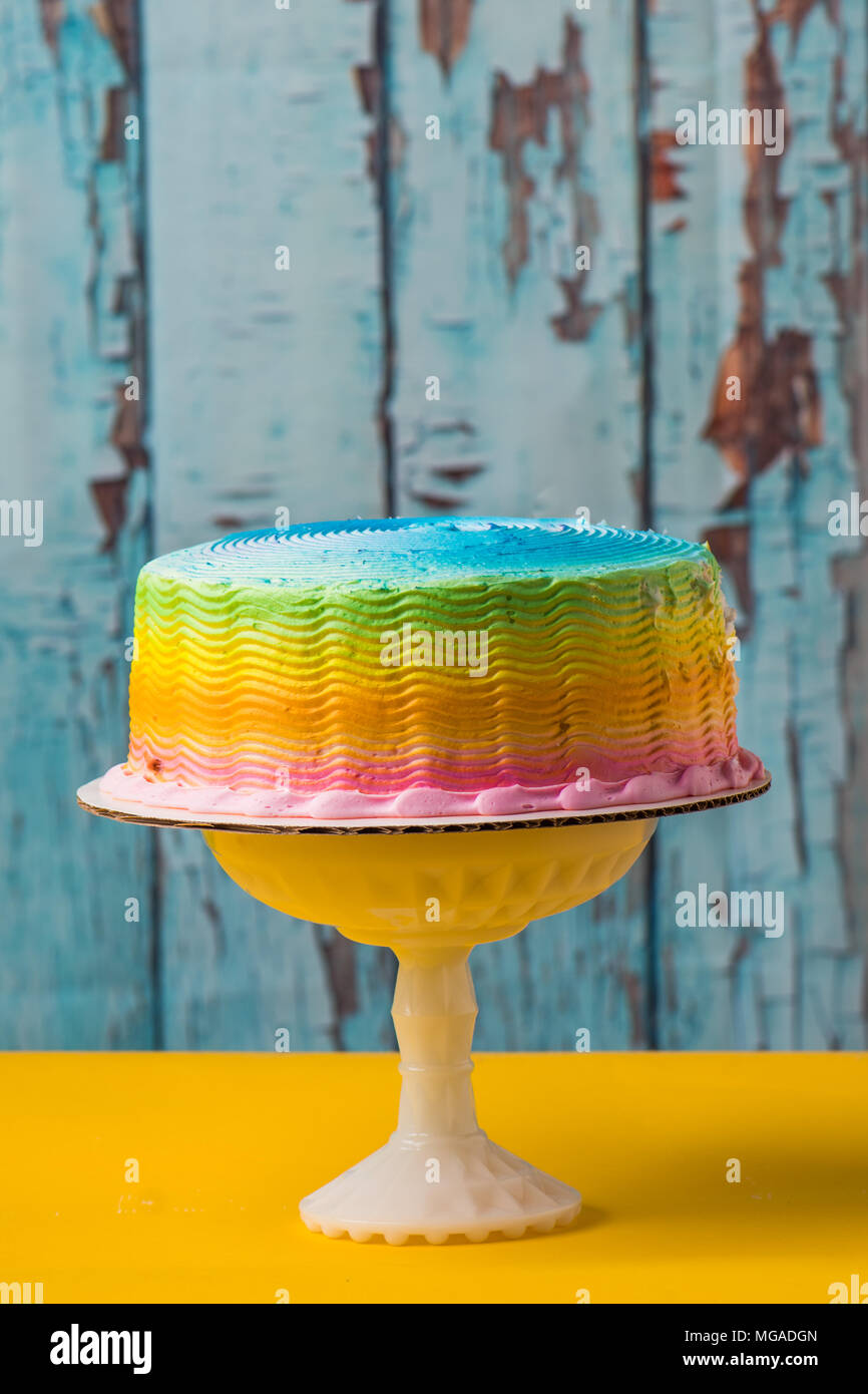Rainbow frosted cake con la tabla de color amarillo y fondo azul Fotografía  de stock - Alamy