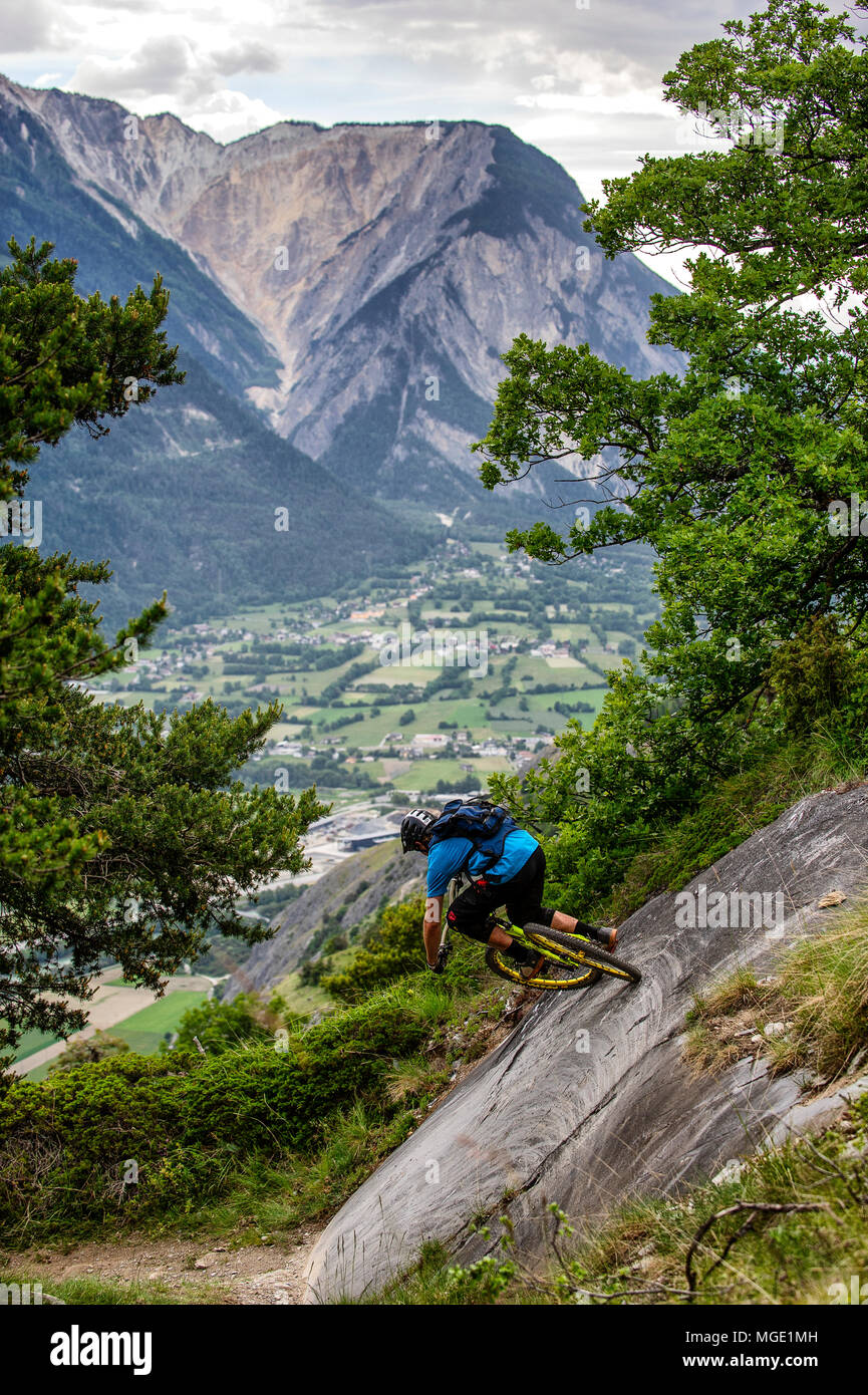 Un hombre monta una bicicleta de montaña de alta sobre el piso del valle, cerca de las localidades de Gampel y Jeizinen en el Valais de Suiza. Foto de stock