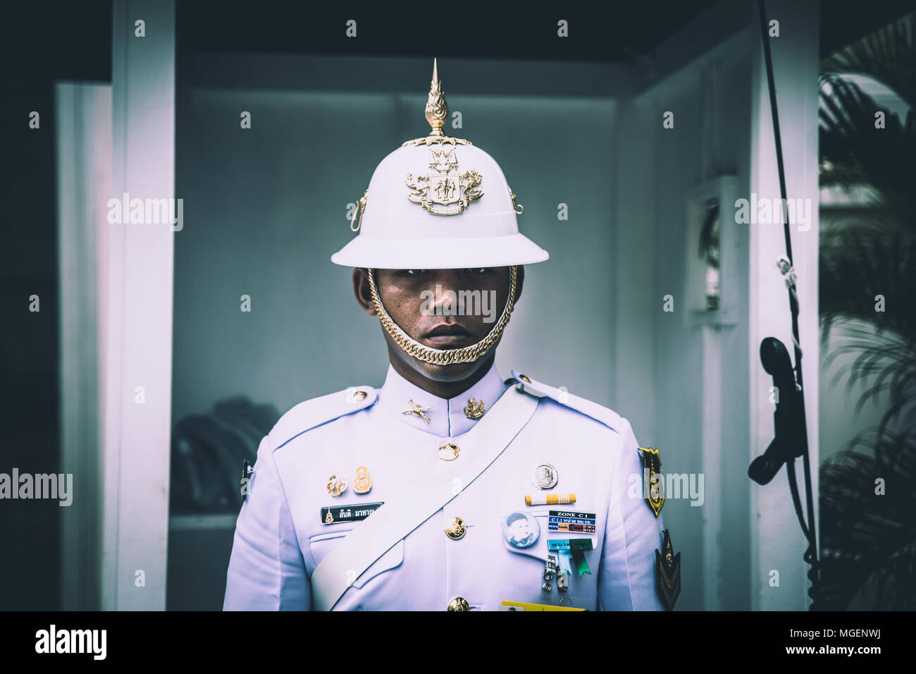Un guardia con rasgos asiáticos vestida de blanco con un decorado timón controla impasible turistas fuera del templo de Wat Pho en Bangkok Foto de stock