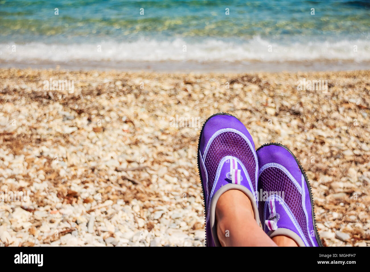 Piernas femeninas con zapatos de neopreno de natación.zapatos acuáticos,  natación patín en neopreno púrpura sobre las rocas en el agua en la playa.  Zapatillas de coral en la playa rocosa Fotografía de