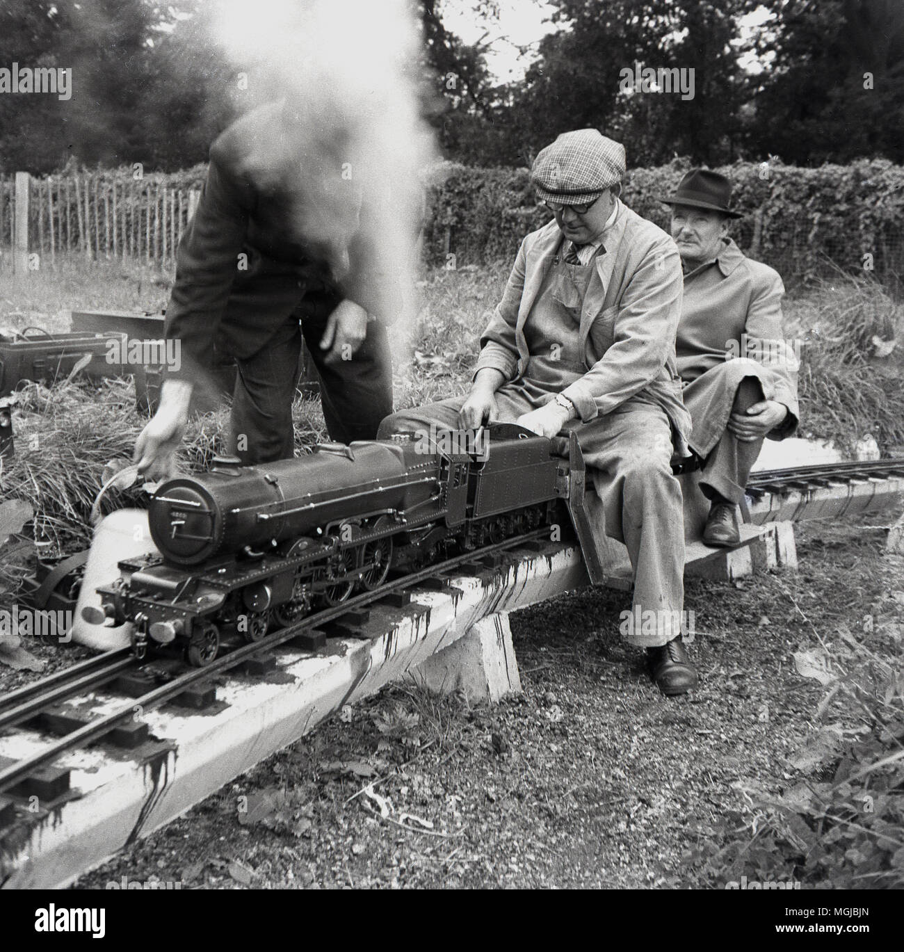 1950s, históricos, macho adulto amteur entusiastas de ferrocarril con un tren de vapor en un trenecito, Inglaterra, Reino Unido. Foto de stock