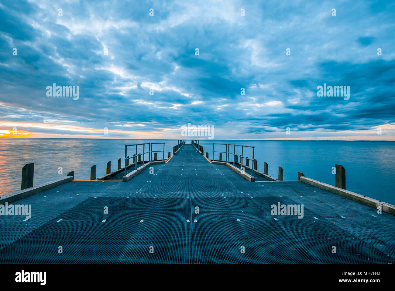 Muelle vacío y calmar las aguas de la bahía bajo el cielo nublado en el  hermoso atardecer Fotografía de stock - Alamy