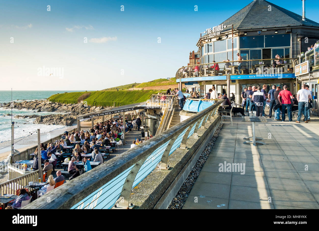 Los turistas que se encuentran en vacaciones en el Fistral Beach Bar disfrutan del sol de la noche en Newquay Cornwall. Foto de stock