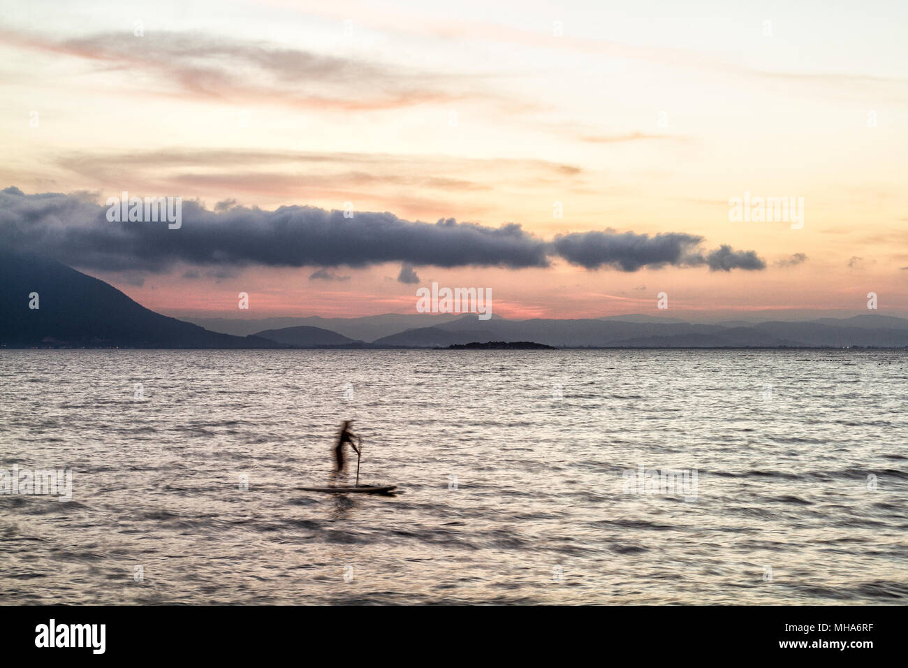 Silueta de una mujer en un stand up paddle board en Ribeirao da Ilha playa al atardecer. La ciudad de Florianópolis, Santa Catarina, Brasil. Foto de stock