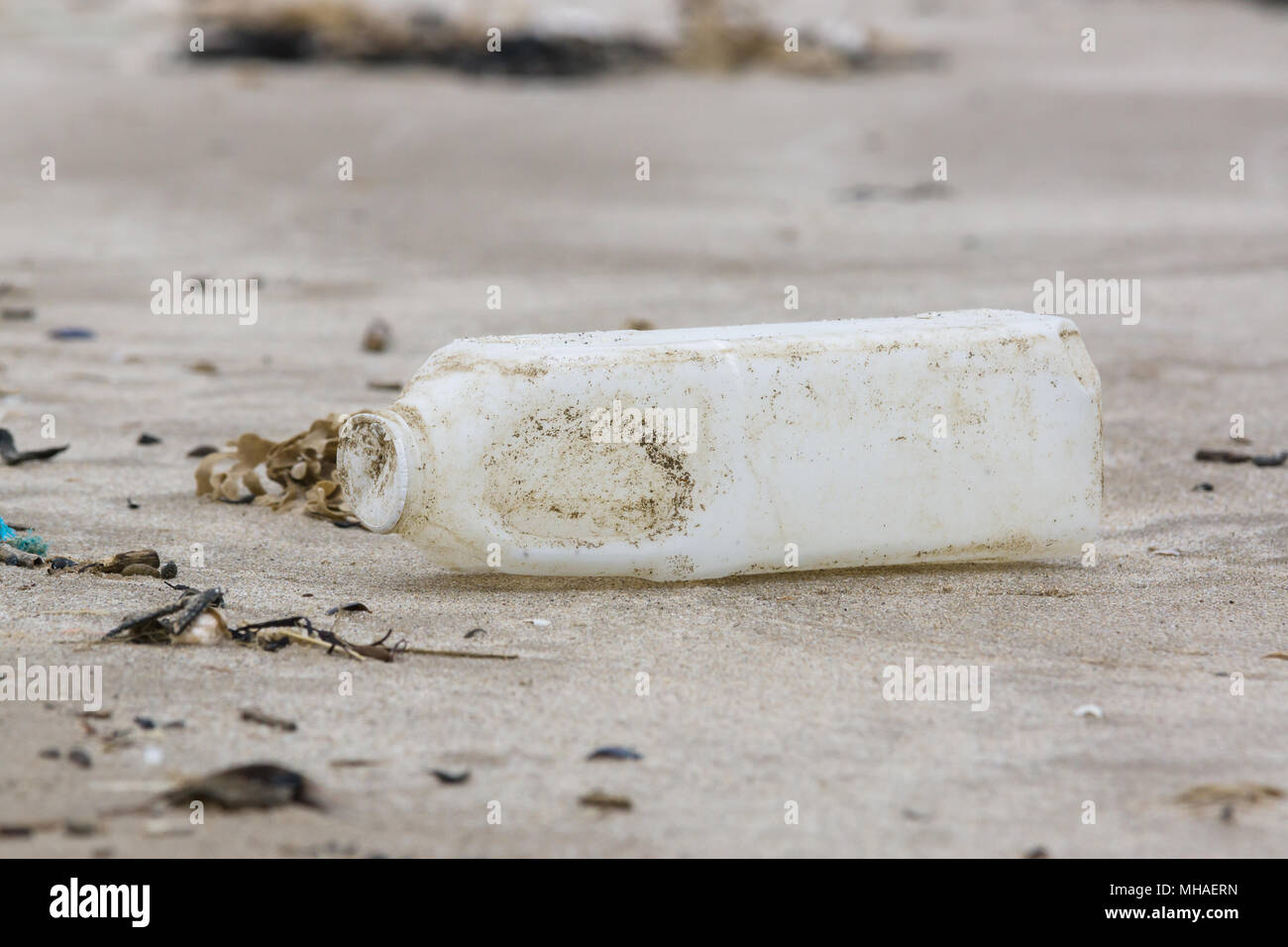Botella de leche de plástico se lavan en una playa de arena, un ejemplo de las muchas piezas de basura en el mar alrededor del Reino Unido Foto de stock