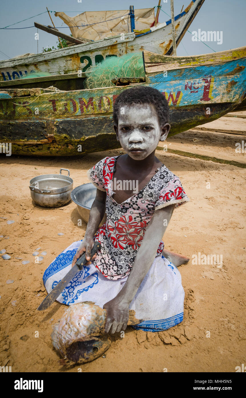 Busua, Ghana - Febrero 04, 2014: jóvenes africanos no identificados chica con el rostro pintado de blanco pescado de corte con machete en la playa Foto de stock