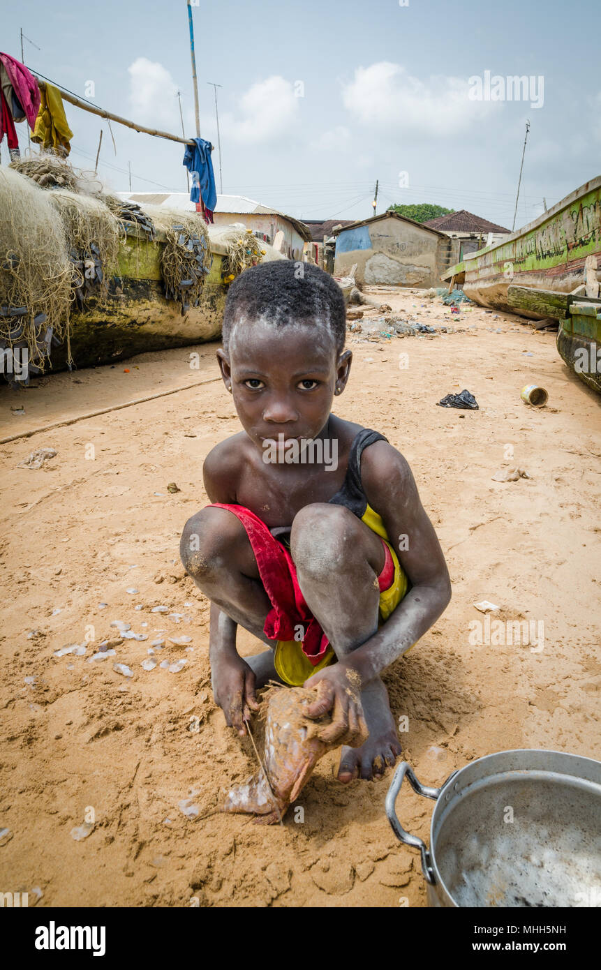 Busua, Ghana - Febrero 04, 2014: jóvenes africanos no identificados chica pescado de corte con machete en la playa Foto de stock