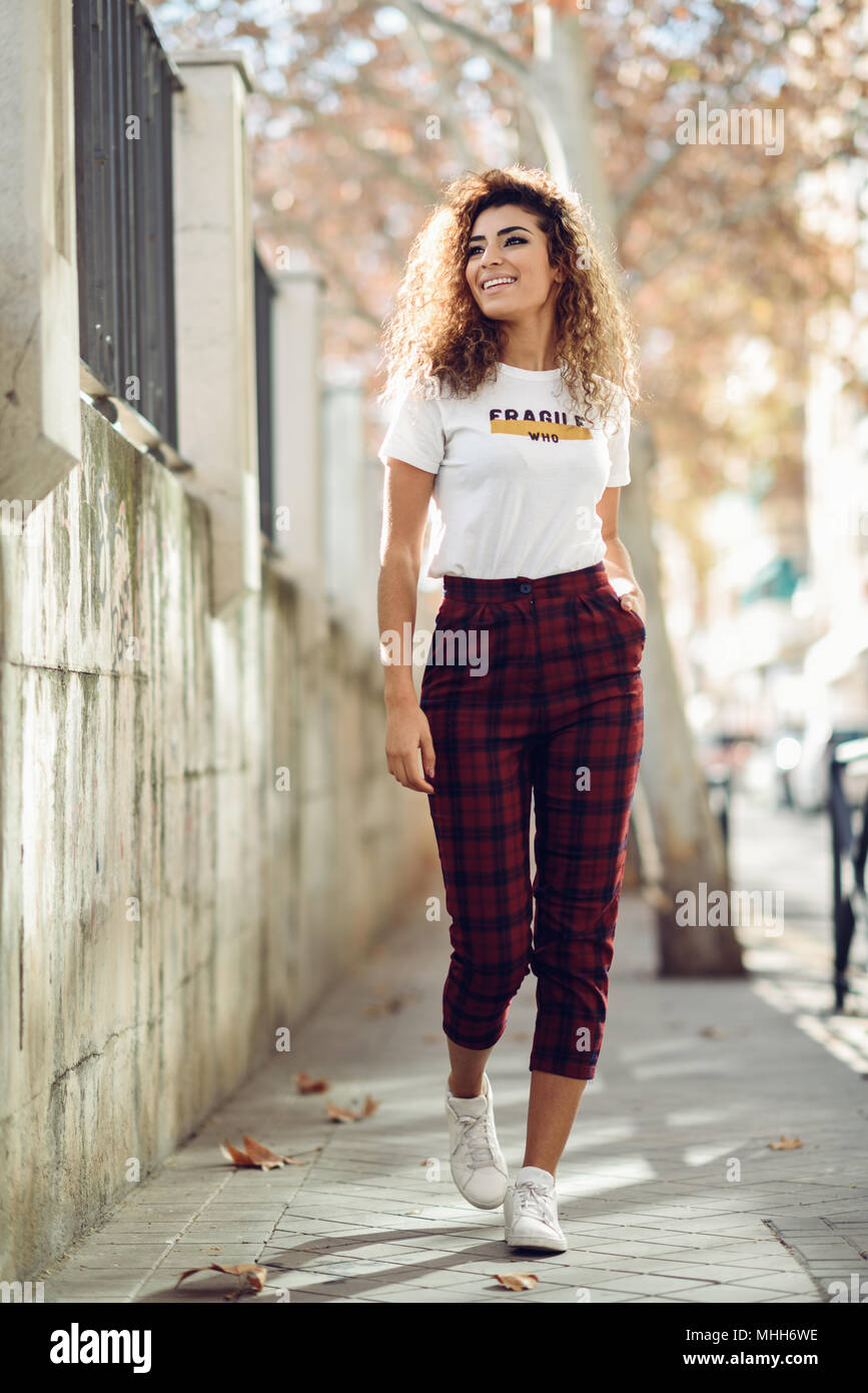 revelación Investigación tifón Joven y bella mujer árabe con peinado rizado negro. Chica árabe en ropa  casual en la calle. Feliz mujeres vistiendo camiseta blanca y chequeo de  pan Fotografía de stock - Alamy