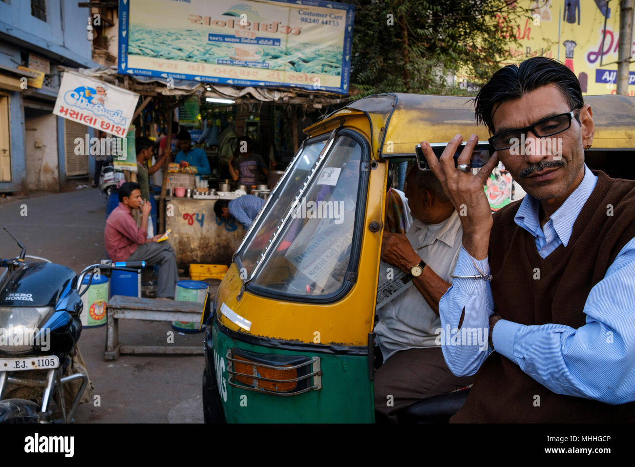 Hombre en el teléfono frente a un tuk tuk. Calle comercial en las atestadas calles de la ciudad vieja de Ahmedabad Manek Chowk. Foto de stock