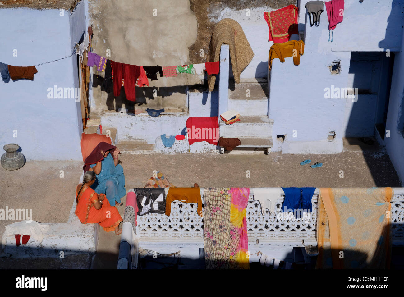Siéntese laundryWomen chateando en el sol como su ropa seca contra las paredes pintadas de azul de Bundi. Rajastán. La India Foto de stock