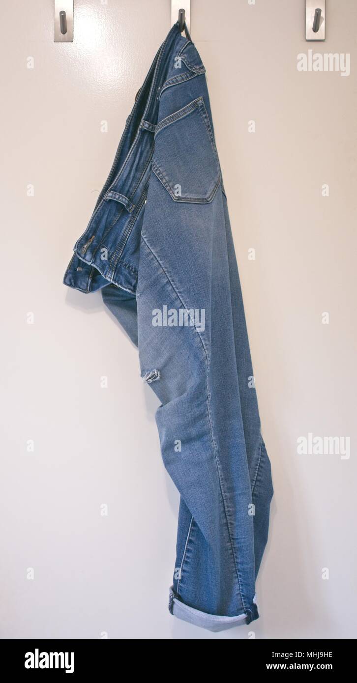 Desgastada, jeans rajados colgando de un gancho en una puerta blanca Foto de stock