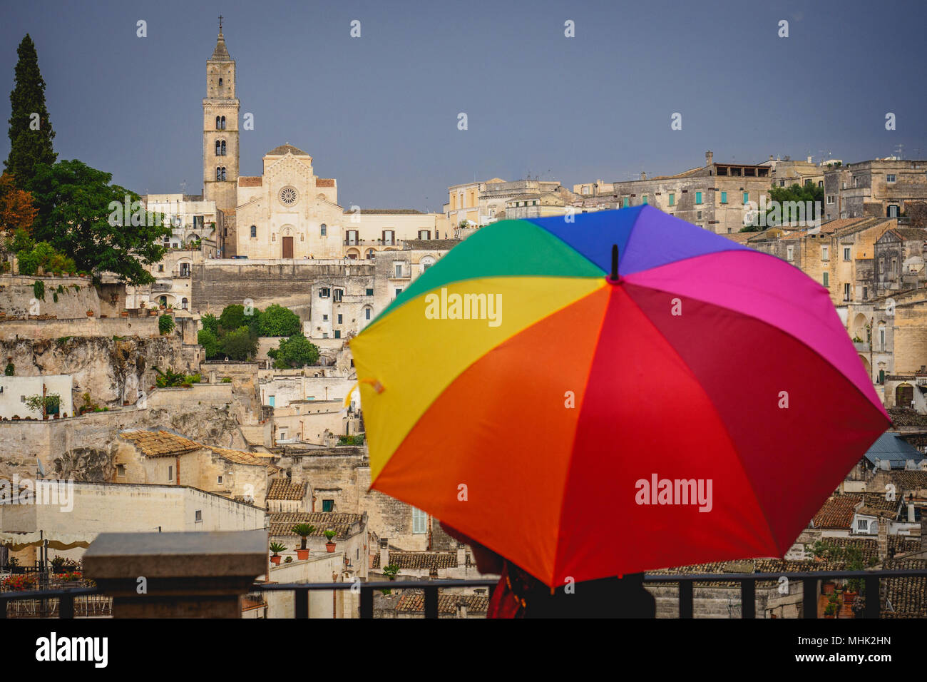 Matera (Italia), en septiembre de 2017. Turista con un paraguas de arco iris en el Belvedere sobre el antiguo pueblo llamado 'Sassi di Matera'. El formato horizontal. Foto de stock