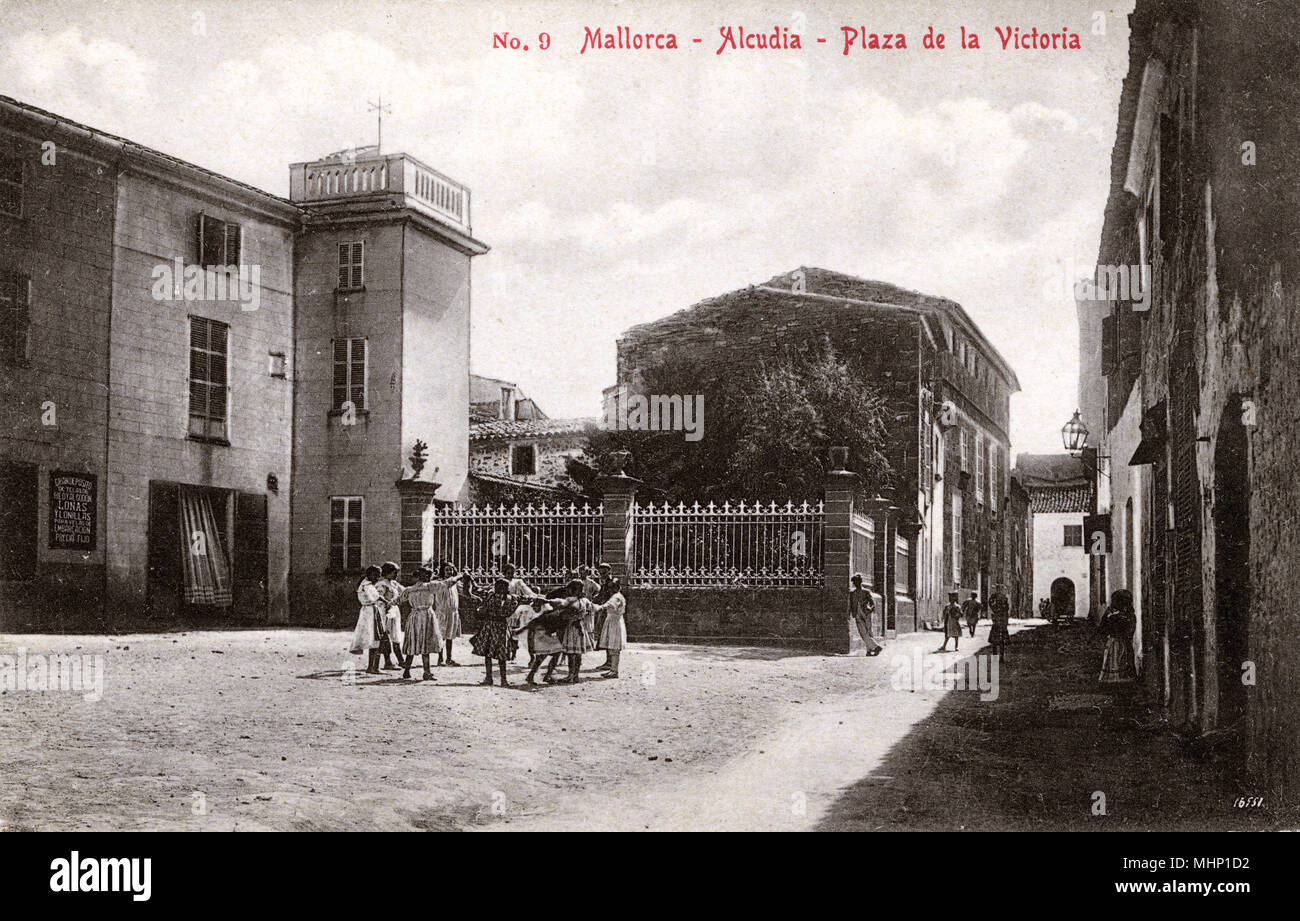 La Plaza de la Victoria, en la ciudad de Alcudia, Mallorca, España, con niños tomados de las manos formando un círculo. Fecha: circa 1910 Foto de stock